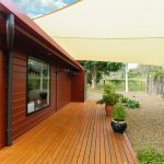 Wooden house with deck, shade sail, and gravel garden