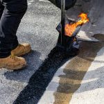 Workers applying hot asphalt with a torch