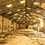 Empty, decaying industrial warehouse with broken roof and debris