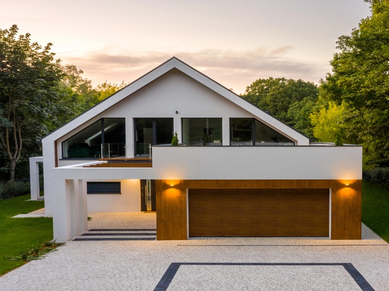 Sunset over elegant white house with forest around, big garage and cobblestone driveway, drone view Sunset over elegant white house with forest around, big garage and cobblestone driveway, drone view