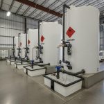 A clean industrial storage area featuring chemical tanks, secure pipe fittings, and visible hazard labels
