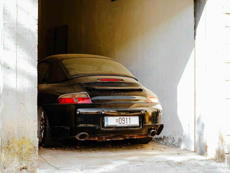 A dusty black sports car parked inside a narrow concrete garage A dusty black sports car parked inside a narrow concrete garage