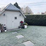 A quaint garden shed surrounded by frosty grass and plants in winter.