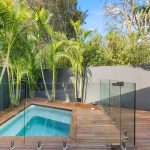 A small plunge pool in a landscaped Australian backyard, with timber decking, greenery, and a compact seating area.