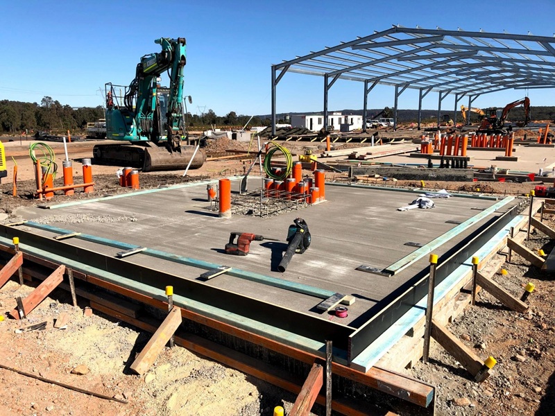 A steel workshop shed under construction, showing the concrete slab, exposed framing, and electrical conduit planning A steel workshop shed under construction, showing the concrete slab, exposed framing, and electrical conduit planning