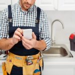 Cropped view of workman in tool belt using smartphone while working in kitchen
