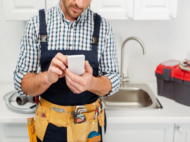 Cropped view of workman in tool belt using smartphone while working in kitchen Cropped view of workman in tool belt using smartphone while working in kitchen